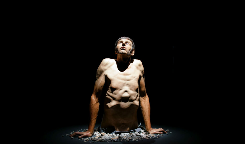 Hyperrealistinen Zharko Basheskin veistos, jossa miehen yläruumis näyttää puskevan maankuoren läpi.