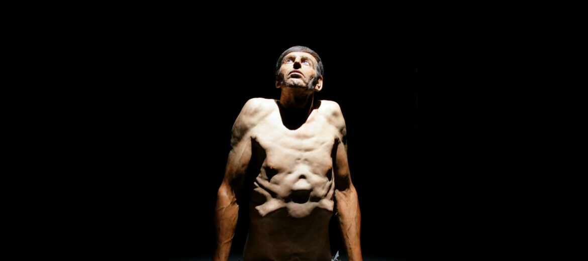 Hyperrealistinen Zharko Basheskin veistos, jossa miehen yläruumis näyttää puskevan maankuoren läpi.